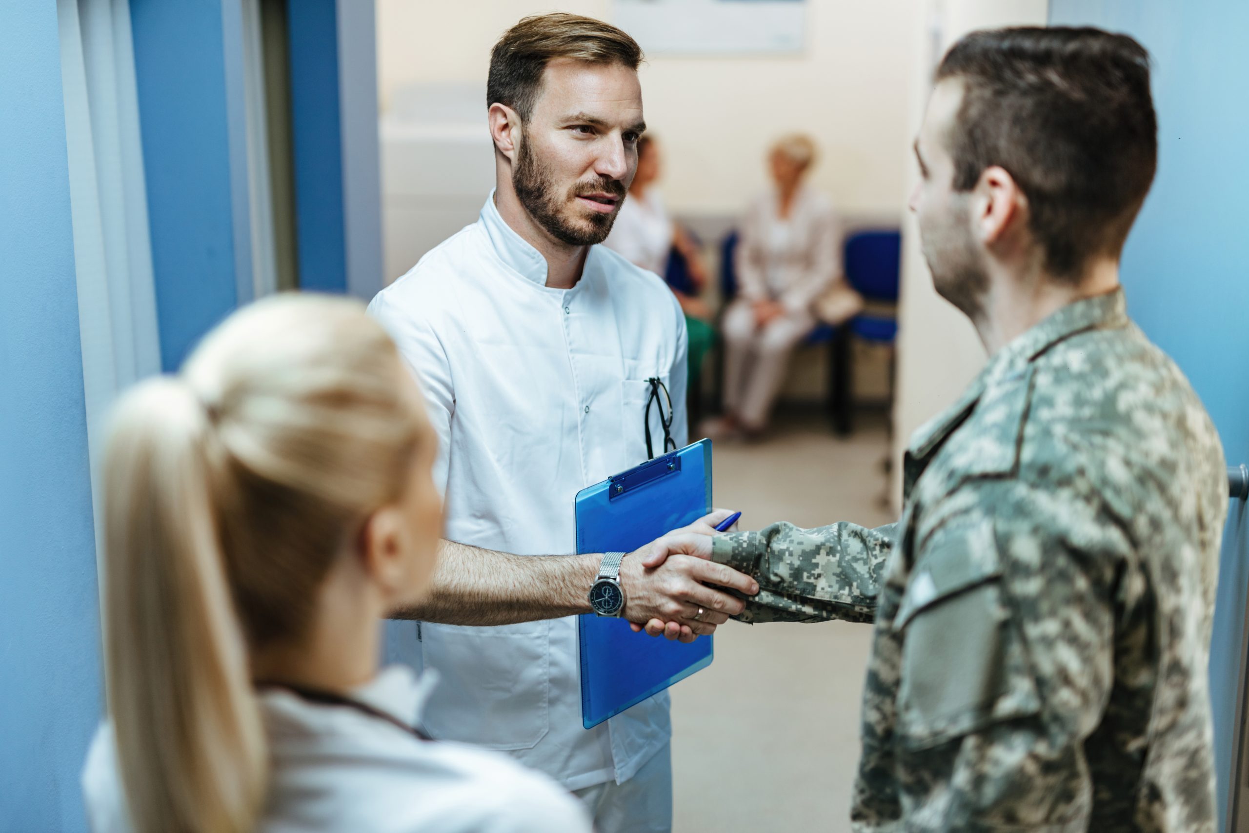 Two doctors talk with military man with one doctor shaking his hand.